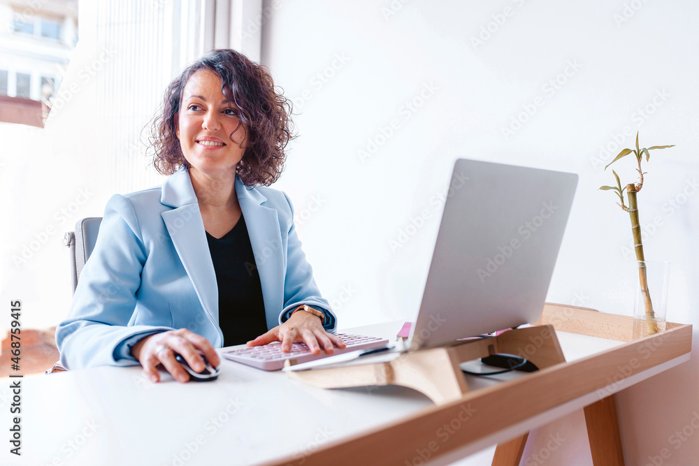 Cheerful woman working on her laptop at the office. Entrepreneur wearing blue suit using technology at work. Business woman, boss, manager, coworker, professional. Business concept. Cheerful woman working on her laptop at the office. Entrepreneur wearing blue suit using technology at work. Business woman, boss, manager, coworker, professional. Business concept.