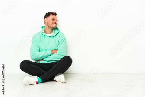 Young handsome caucasian man sitting on the floor looking side