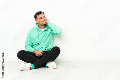 Young handsome caucasian man sitting on the floor thinking an idea