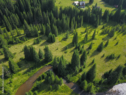 Drone view above Frumoasa valley. The river winds through beautiful meadows and spruce trees. Several cabins are built in the alpine pastures. Carpathia, Romania. photo