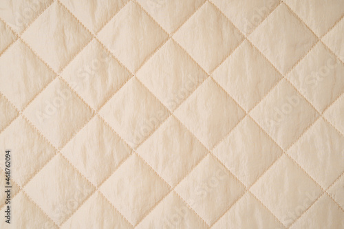 Quilted fabric background. Beige  texture blanket or puffer jacket photo