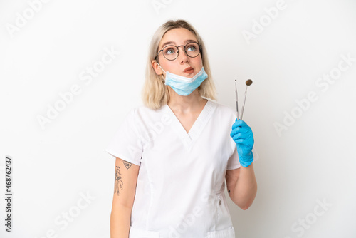 Dentist caucasian woman holding tools isolated on white background and looking up
