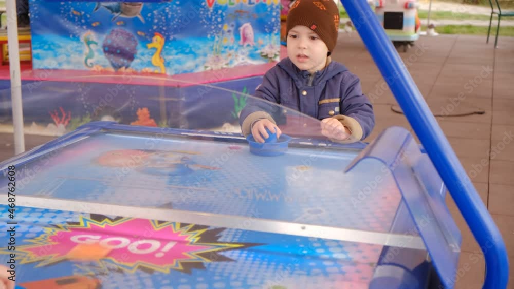 The child plays air hockey outdoors and talks. The child plays air hockey outdoors and talks.