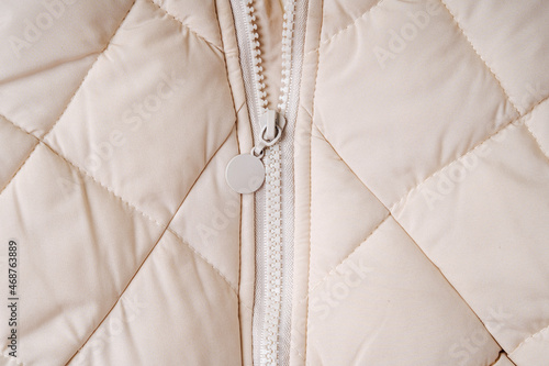 Close-up on beige puffer jacket texture with zipper. Quilted fabric background