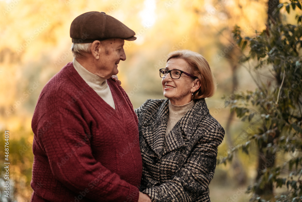 Elderly man looking at his elegant retired woman with love, warming her hands and enjoying her beauty, senior married couple dancing in autumn park, celebrating anniversary, affection Elderly man looking at his elegant retired woman with love, warming her hands and enjoying her beauty, senior married couple dancing in autumn park, celebrating anniversary, affection