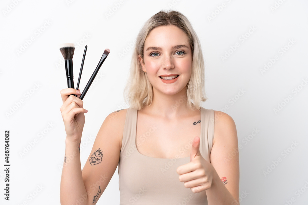 Young caucasian woman isolated on white background holding makeup brush and with thumb up