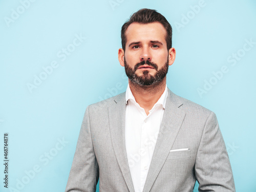 Portrait of handsome confident stylish hipster lambersexual model.Sexy modern man dressed in elegant suit. Fashion male posing in studio near blue wall