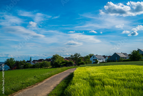 Germany, Dreamy houses and church steeple of village ostfildern kemnat behind curved way and green fields in summer