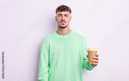 young handsome man feeling sad and whiney with an unhappy look and crying. take away coffee concept photo