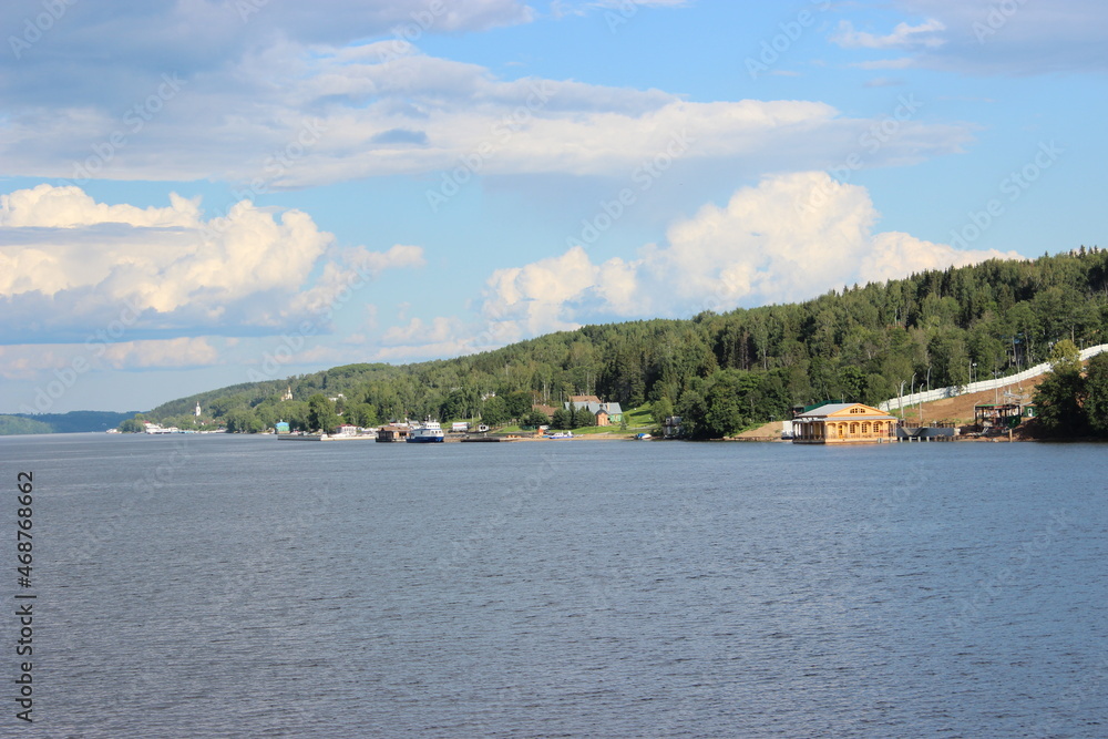 Volga River in summer - the vicinity of the city of Ples, view from the ship. Houses and other buildings on the shore between the trees.