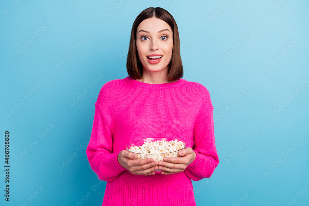 Photo of shiny excited young lady wear pink pullover smiling eating pop corn isolated blue color background Photo of shiny excited young lady wear pink pullover smiling eating pop corn isolated blue color background