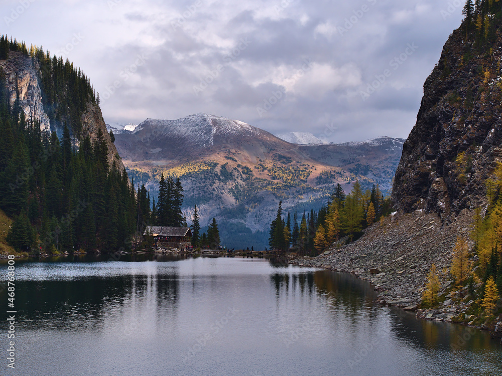 View of Lake Agnes in autumn with yellow colored larch trees and hikers at the tea house in valley in the Rocky Mountains, Banff National Park, Canada.