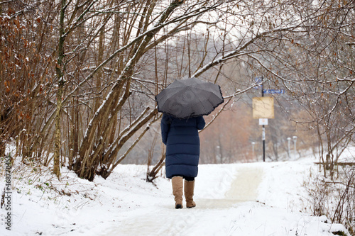 Snow with rain, woman with umbrella walking in a city park