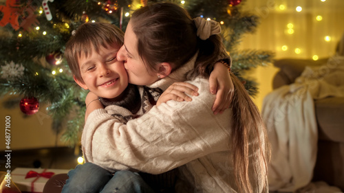 Portrait of happy mother kissing her smiling son in cheek while celebrating Christmas or New Year