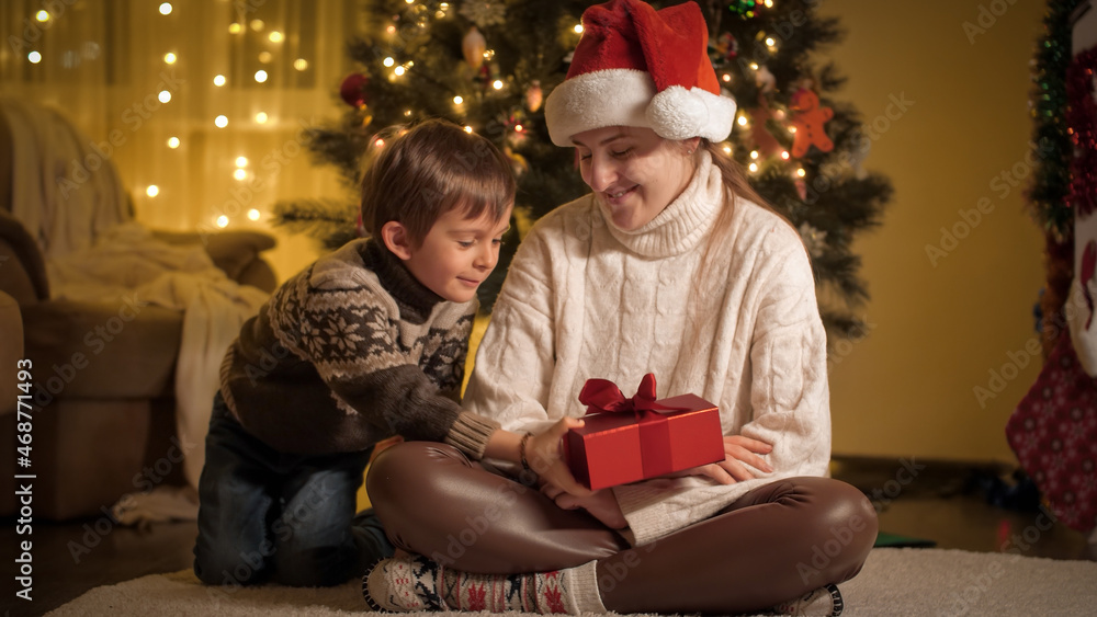 Cheerful smiling boy with mother giving Christmas presents and hugging under Christmas tree at house. Families and children celebrating winter holidays. Cheerful smiling boy with mother giving Christmas presents and hugging under Christmas tree at house. Families and children celebrating winter holidays.