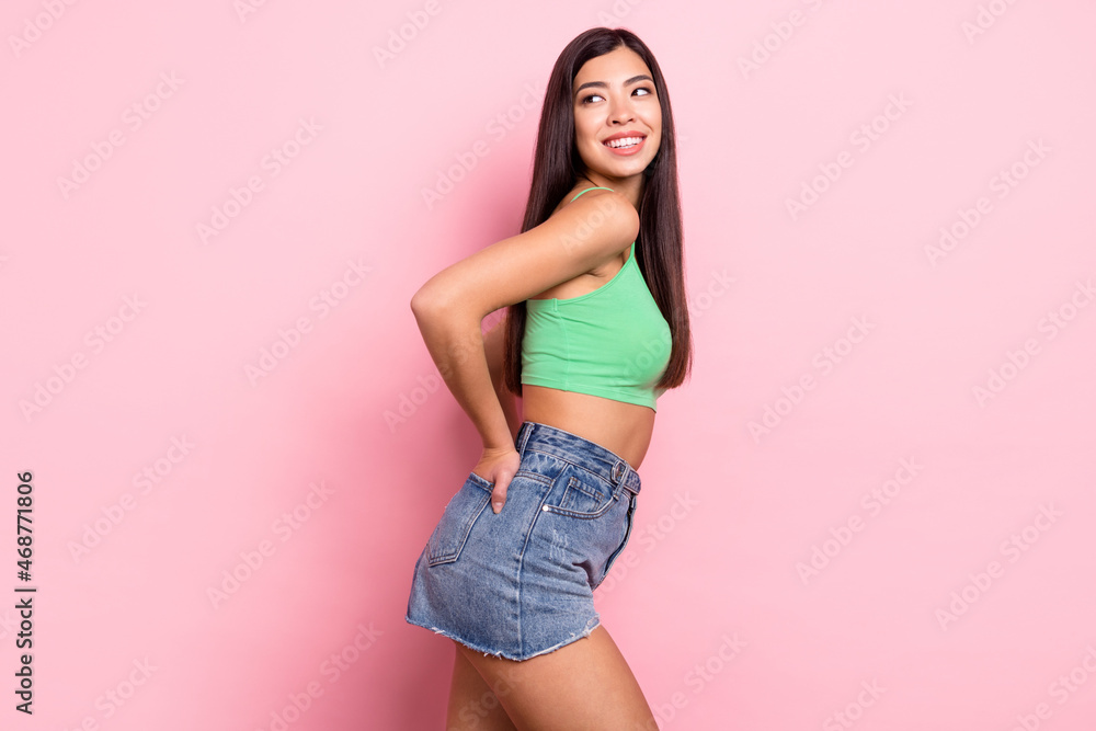 Photo of charming pretty woman hair dressed green singlet smiling arms pockets looking back empty space isolated pink color background Photo of charming pretty woman hair dressed green singlet smiling arms pockets looking back empty space isolated pink color background