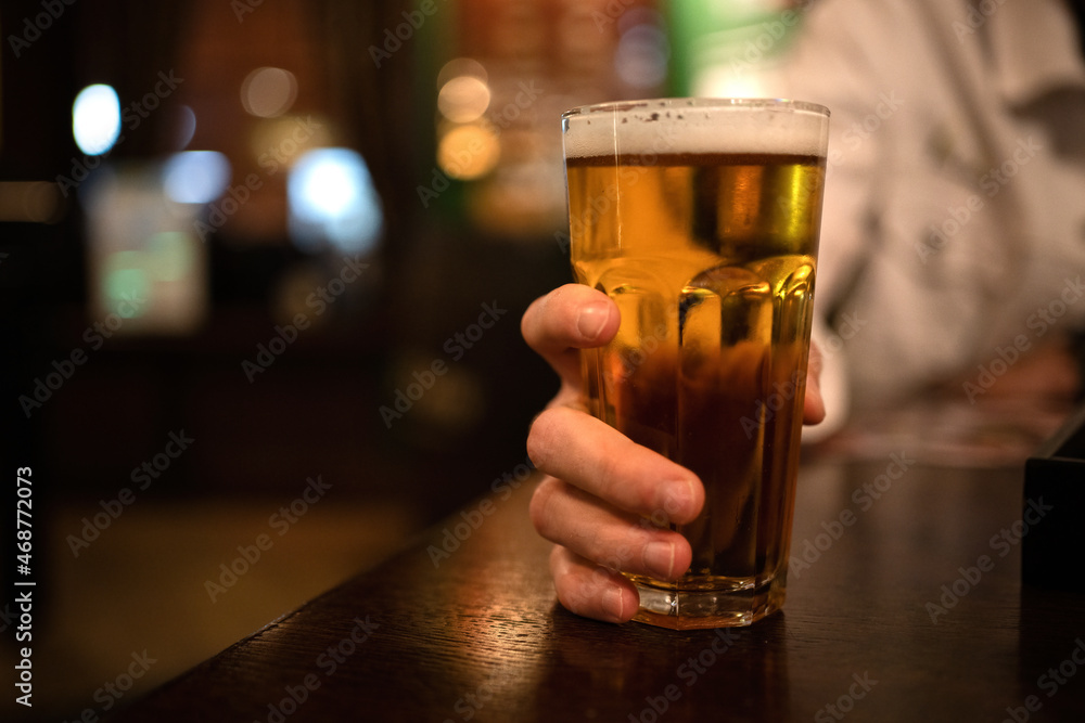 A glass of beer in the hand of a man in a bar.