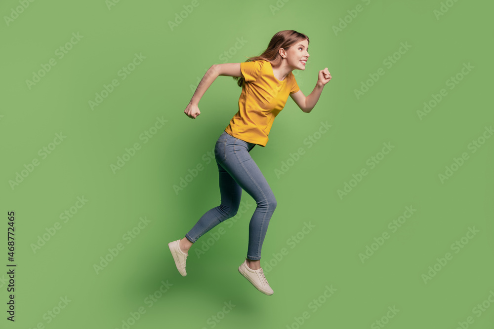 Profile portrait of pretty energetic lady jump run wear yellow t-shirt jeans sneakers on green background Profile portrait of pretty energetic lady jump run wear yellow t-shirt jeans sneakers on green background