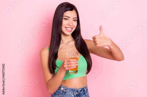 Photo of confident pretty young woman hair dressed green singlet holding juice shoving thumb up isolated pink color background © deagreez