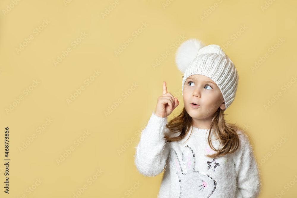 Portrait child girl with finger pointed up. Little kid in winter knitted hat with pompon pose has idea isolated yellow background. Christmas New Year shopping sale,promotion.celebration holiday party Portrait child girl with finger pointed up. Little kid in winter knitted hat with pompon pose has idea isolated yellow background. Christmas New Year shopping sale,promotion.celebration holiday party