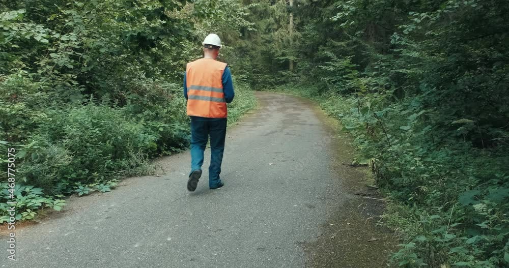 Worker in workwear and a helmet on a highway in the forest. The concept of repairing roads, a fallen tree and an accident on a forest, country road Worker in workwear and a helmet on a highway in the forest. The concept of repairing roads, a fallen tree and an accident on a forest, country road