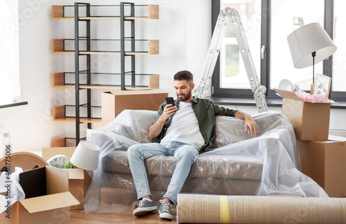 moving, people and real estate concept - man with smartphone and boxes at new home