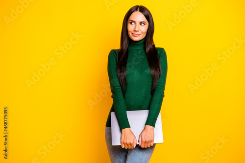 Photo of charming calm young brunette woman look empty space hold hands laptop isolated on yellow color background