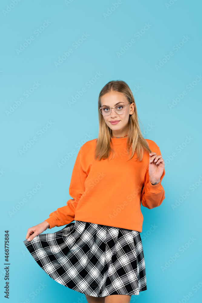 Blonde student holding skirt and looking at camera isolated on blue Blonde student holding skirt and looking at camera isolated on blue