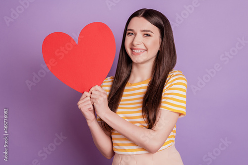 Portrait of adorable sweet lady showing big red paper heart white smile on purple background © Tetiana