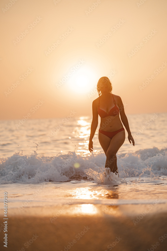 Silhouette of the woman walking out of the sea in the sunlight of the sunset