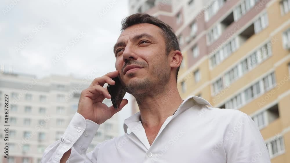 Handsome businessman speaks on the phone with a smile. Young man in the city center against the background of high-rise buildings. The concept of business and professional activities. 4K UHD. Handsome businessman speaks on the phone with a smile. Young man in the city center against the background of high-rise buildings. The concept of business and professional activities. 4K UHD.