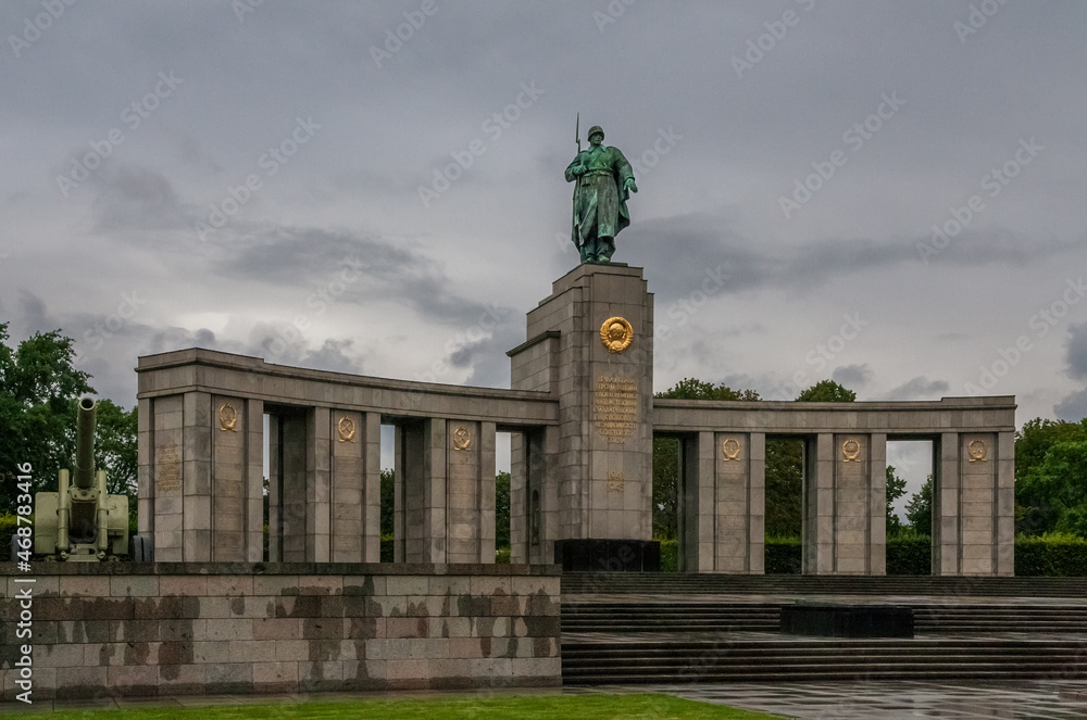 Fototapeta premium The Soviet War Memorial in the park Tiergarten in Berlin, the capital city of Germany on a rainy, gloomy day. Next to the curved stoa with a Soviet soldier is a Red Army ML-20 152mm howitzer-gun.
