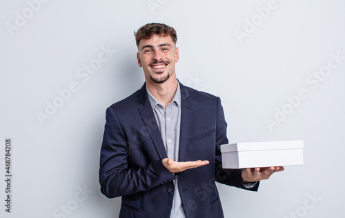 young handsome man smiling cheerfully, feeling happy and showing a concept. white box package