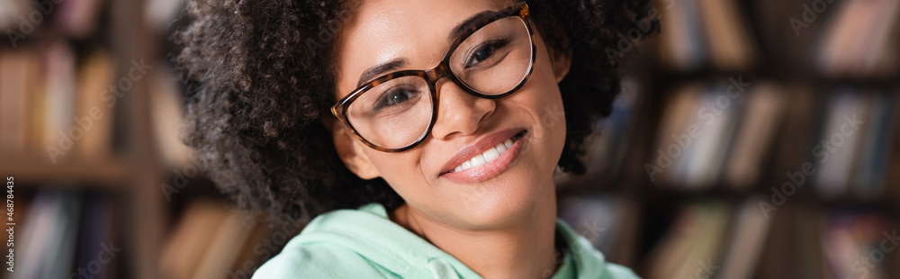 cheerful african american woman in eyeglasses looking at camera, banner