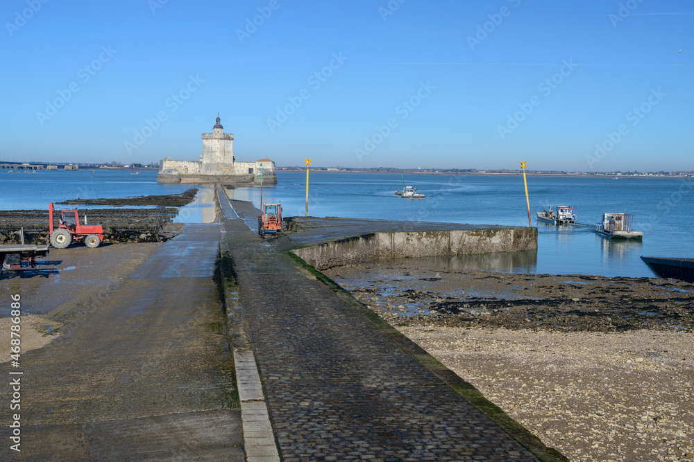 Oyster beds on causeway to ancient Fort Louvois fortified tower with oyster farming boats leaving port on Atlantic coast of Charente Maritime, France