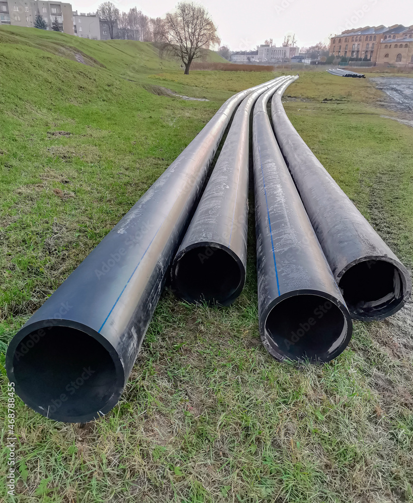 Large-diameter plastic pipes lie on the ground surface before installation.