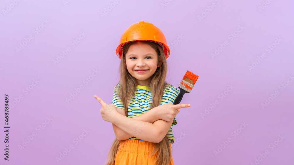 A little girl in a construction helmet and a paint brush in her hands. she points her fingers in different directions. A little girl in a construction helmet and a paint brush in her hands. she points her fingers in different directions.