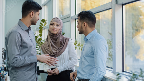 Multiethnic colleagues arab muslim woman in hijab and two Indian millennial male discuss corporate task. Diverse workers businesspeople working together in modern office, teamwork brainstorm concept