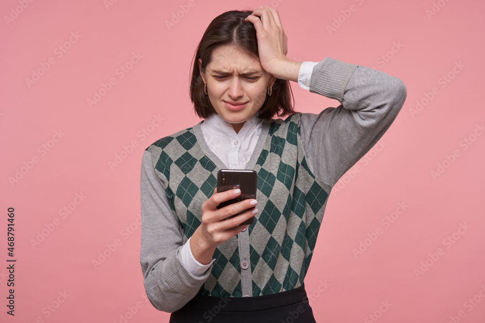 Indoor portrait of young sad unhappy female student, keeps her hand on head while reading bad news . Isolated over pink background Indoor portrait of young sad unhappy female student, keeps her hand on head while reading bad news . Isolated over pink background