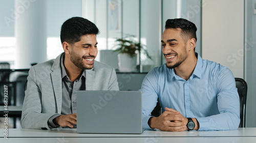 Cheerful smiling male colleagues employees cooperating in office talking working together at workplace, optimistic businessmen coworkers discussing business project celebrating good teamwork results