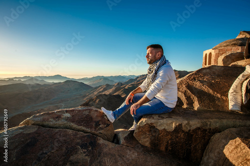 A man sits facing the rising sun on Mount Sinai in Egypt.