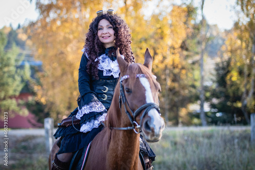 Half-lenght portrait of a mature woman in a steampunk costume on a horse against the backdrop of an autumn landscape.