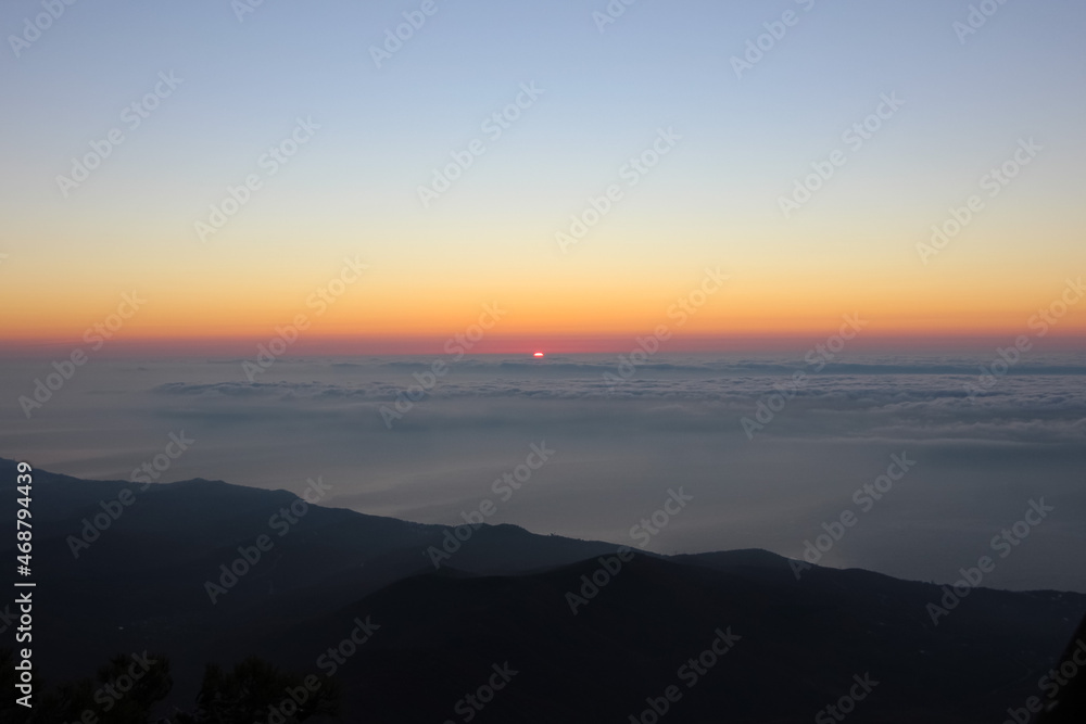 Sunrise seen from the mountains. Sun on the horizon above the clouds