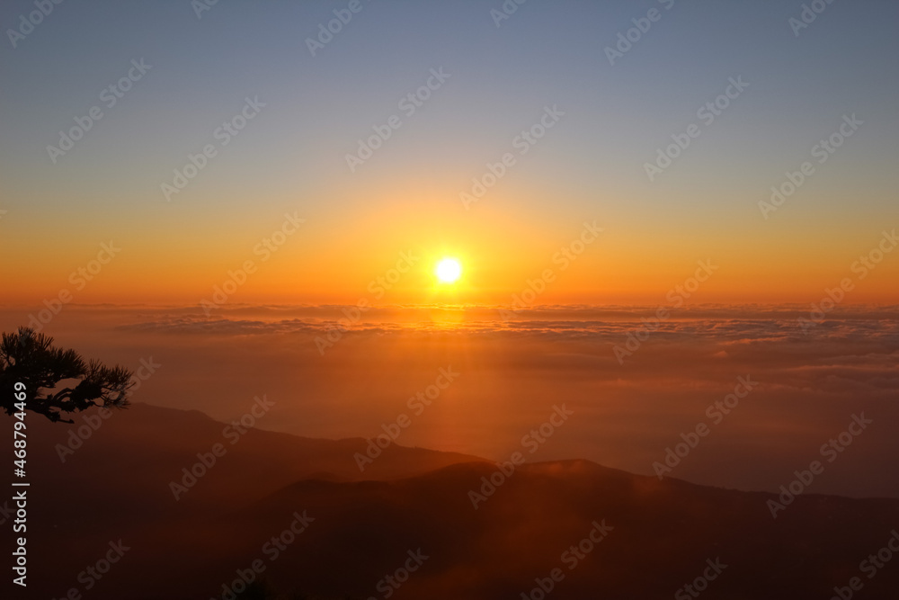 View from the top at sunrise in the mountains. Sun disk on the horizon above the clouds