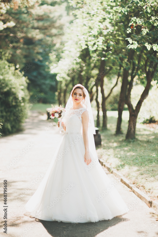 Beautiful luxury young bride in wedding dress posing in park