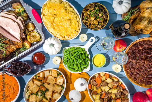 Thanksgiving dinner table with new traditional thanksgiving food - chicken, mashed sweet potatoes, green beans, pecan pie, baked ham pork, mac and cheese, stuffing, modern hard sunny light flatlay