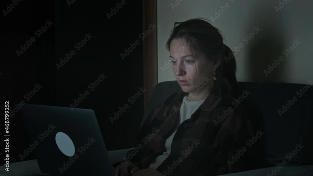 Young adult caucasian woman sitting on couch near her bed and working with her laptop computer late at night. Young adult caucasian woman sitting on couch near her bed and working with her laptop computer late at night.
