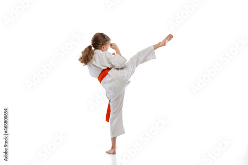 Portrait of little girl, young karate training alone isolated over white background. Concept of sport, education, skills