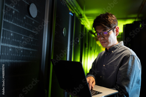 Asian male engineer using laptop in computer server room