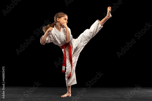 Portrait of little girl, young karate practicing alone isolated over dark background. Concept of sport, education, skills